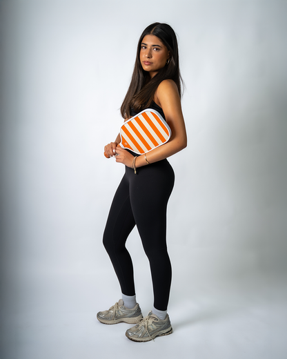 Woman holding an orange and white striped Pickleball Paddle against a plain background